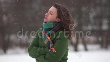 美丽的年轻女子享受着降雪，无所畏惧。 穿着绿色外套和围巾，冬天在公园散步